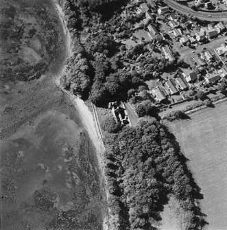 Oblique aerial view centred on the church and burial ground with pier adjacent, taken from the E.