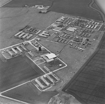 Oblique aerial view of Crail Airfield centred on the remains of buildings, a water tank and a hut, taken from the NNE.