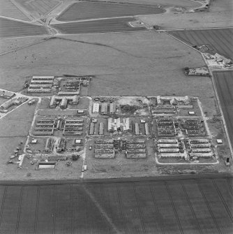 Oblique aerial view of Crail Airfield centred on the remains of buildings, a water tank and a hut, taken from the NW.