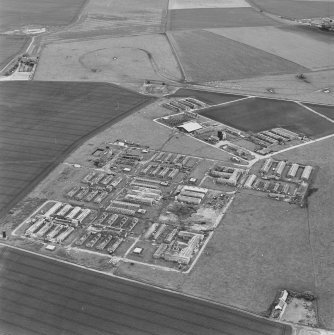 Oblique aerial view of Crail Airfield centred on the remains of buildings, a water tank and a hut, taken from the SSW.