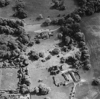 Oblique aerial view of Mountquhanie House centred on the country house, 'dovecot', stables and the remains of a castle, taken from the NNW.
