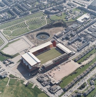 Oblique aerial view centred on the stadium, with the cemetery adjacent, taken from the NE.