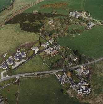 Oblique aerial view of the village centred on the burial-ground, manse and the remains of the church with the farmsteading adjacent, taken from the SW.
