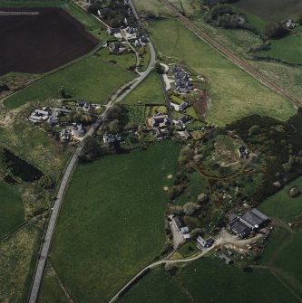 Oblique aerial view of the village centred on the burial-ground, manse and the remains of the church with the farmsteading adjacent, taken from the ESE.