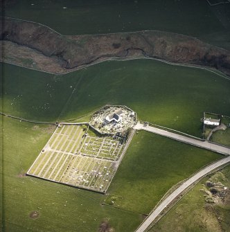 Oblique aerial view centred on the church and burial-ground with the farmstead adjacent, taken from the NE.