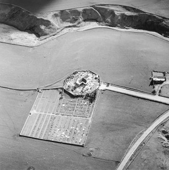 Oblique aerial view centred on the church and burial-ground with the farmstead adjacent, taken from the NE.