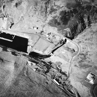 Oblique aerial view centred on the harbour and lighthouse with the warehouses and road bridge adjacent, taken from the ENE.