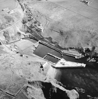 Oblique aerial view centred on the harbour and lighthouse with the warehouses and road bridge adjacent, taken from the WSW.