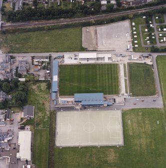 Oblique aerial view centred on the football stadium with courthouse and police station adjacent, taken from the ESE.