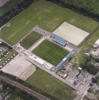 Oblique aerial view centred on the football stadium with courthouse and police station adjacent, taken from the WSW.