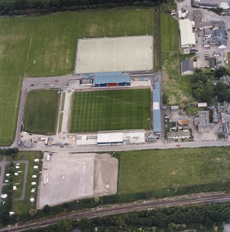 Oblique aerial view centred on the football stadium with courthouse, police station and hospital adjacent, taken from the WNW.