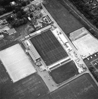 Oblique aerial view centred on the football stadium with courthouse and police station adjacent, taken from the NE.