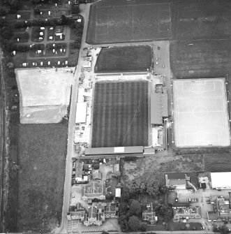 Oblique aerial view centred on the football stadium with courthouse and police station adjacent, taken from the SSW.