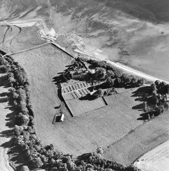 Oblique aerial view centred on the church, burial ground, farmsteading and barn with saltings adjacent, taken from the N.