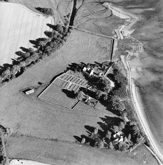 Oblique aerial view centred on the church, burial ground, farmsteading and barn with saltings adjacent, taken from the WNW.