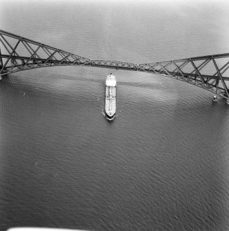 Aerial view of a cargo ship passing underneath a central girder of the bridge.