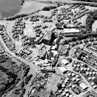 Oblique aerial view of former distillery, taken from ENE, with Saladin-box maltings in the centre left, floor-maltings and kilns to centre right, and malt-extract buildings and boiler house (with chimney) in foreground.