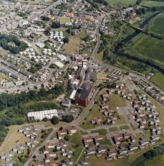 Oblique aerial view of former distillery, taken from WSW, with Saladin-box maltings to centre right and floor-maltings with two kilns to centre left