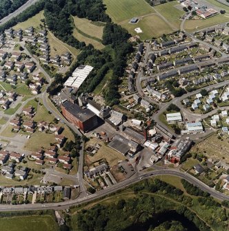 Oblique aerial view of former distillery, taken from ESE, with Saladin-box maltings in the foreground left and malt-extract buildings to the right.