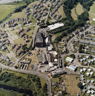 Oblique aerial view of former distillery, taken from ENE, with Saladin-box maltings in the centre left, floor-maltings and kilns to centre right, and malt-extract buildings and boiler house (with chimney) in foreground.