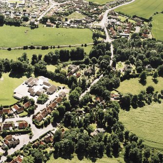 Oblique aerial view centred on the church and burial ground with villages adjacent, taken from the NE.