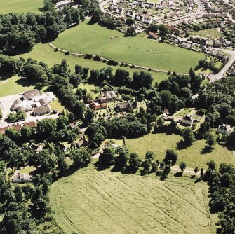 Oblique aerial view centred on the church and burial ground with villages adjacent, taken from the N.