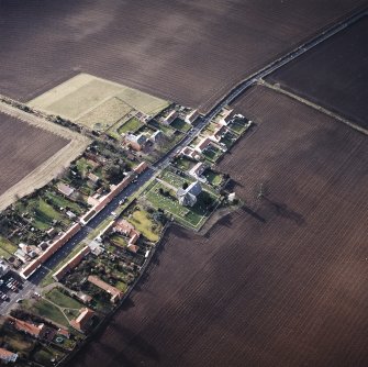 Oblique aerial view of the village centred on the church, burial-ground and burial-enclosure, taken from the NE.