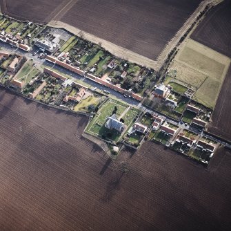 Oblique aerial view of the village centred on the church, burial-ground and burial-enclosure, taken from the NW.
