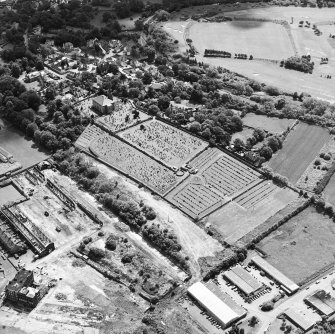 Oblique aerial view centred on the church and burial ground with remains of works adjacent, taken from the NW.