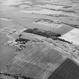 Oblique aerial view centred on the road construction and the quarry, with the farmhouses, farmsteading and cottages adjacent, taken from the SE.