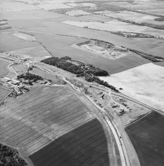 Oblique aerial view centred on the road construction and the quarry, with the farmhouses, farmsteading and cottages adjacent, taken from the ESE.