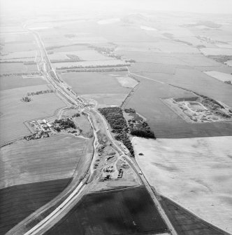 Oblique aerial view centred on the road construction with the quarry, farmhouse, farmsteading and cottages adjacent, taken from the E.
