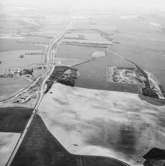 Oblique aerial view centred on the road construction with the quarry, farmhouse, farmsteading and cottages adjacent, taken from the ENE.