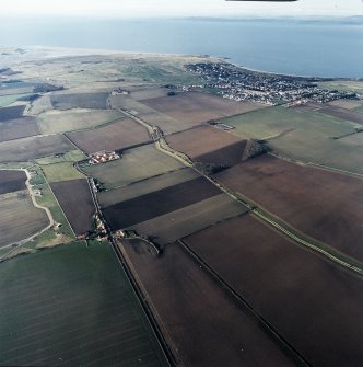 General oblique aerial view looking across the modern amalgamated fields, farmhouse, farmsteading and village towards the golf course and the Firth of Forth, taken from the E.