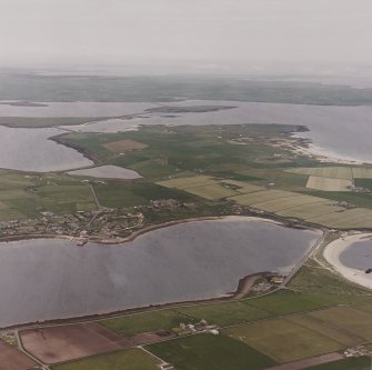 Oblique aerial view from S, centred on the island of Burray and showing Burray Village in the centre left of the photograph, and Churchill Barrier No. 4 in the right centre. N Cara Mound is visible in the centre foreground.