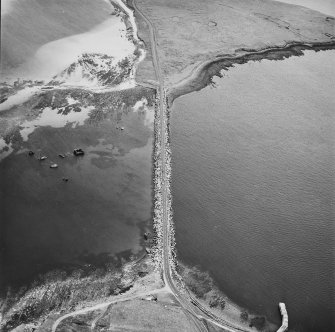 Oblique aerial view from NE, centred on the Barrier, and showing the wreck of the blockship Elton in the centre left of the photograph, and traces of Air-raid Shelters and a Tramway on Glimps Holm in the top right-hand corner.