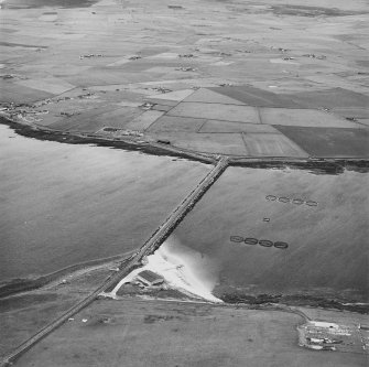 Oblique aerial view from SE, centred on the Barrier, and showing the remains of Lamb Holm Military Camp in the bottom right-hand corner of the photograph.