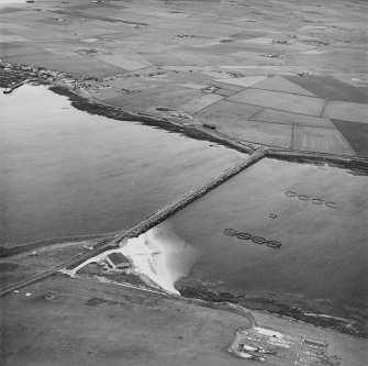 Oblique aerial view from ESE, centred on the Barrier, and showing The Italian Chapel, and the remains of Lamb Holm Military Camp, in the bottom right-hand corner of the photograph.