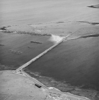 Oblique aerial view from NW, centred on the Barrier, and showing the remains of Lamb Holm Military Camp and Coast Battery in the top half of the photograph.