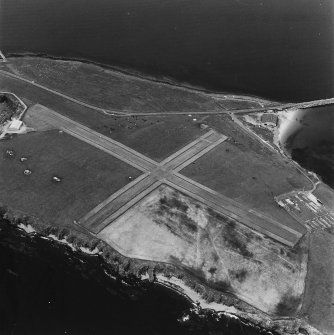 Oblique aerial view, Orkney, Lamb Holm taken from the SE.  Visible is the modern grass landing strip, Lamb Holm World War II coast battery, the concrete hut bases of the former prisoner-of-war camp, the Italian Chapel and part of Churchill Barrier No.1.