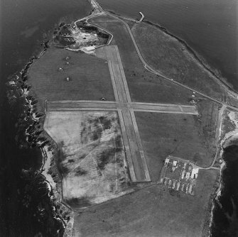 Oblique aerial view, Orkney, Lamb Holm taken from the NE.  Visible is the modern grass landing strip, Lamb Holm World War II coast battery, the concrete hut bases of the former prisoner-of-war camp, the Italian Chapel and part of Churchill Barrier No.2.