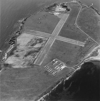 Oblique aerial view, Orkney, Lamb Holm taken from the NNE.  Visible is the modern grass landing strip, Lamb Holm World War II coast battery, the concrete hut bases of the former prisoner-of-war camp, the Italian Chapel.