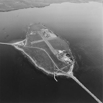 Aerial view, Orkney, Lamb Holm taken from the W.  Visible is the modern grass landing strip, Lamb Holm World War II coast battery, the concrete hut bases of the former prisoner-of-war camp, the Italian Chapel and parts of Churchill Barriers Nos. 1 and 2.