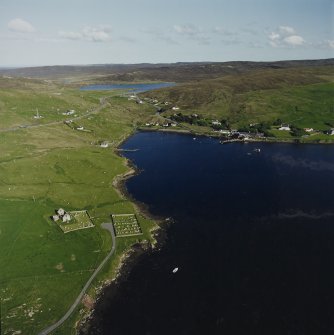 Oblique aerial view looking across Olna Firth to the village of Voe centred on the remains of the burial ground, church and churchyard, taken from the NW.