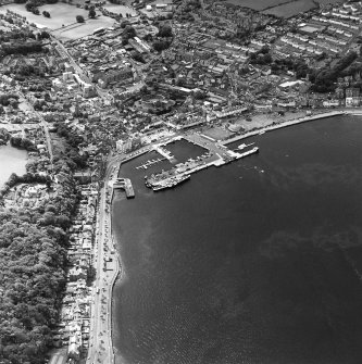 Oblique aerial view of Rothesay, taken from the NE, centred on a harbour.  A castle and the Winter Gardens are visible, in the top centre and centre of the photograph, respectively.