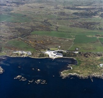 Oblique aerial view centred on the whisky distillery, pier and cottages with the remains of the castle adjacent, taken from the SSE.