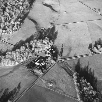 Oblique aerial view centred on the farmstead and school, with the remains of the cairns adjacent, taken from the SSW.