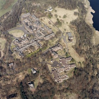 Oblique aerial view centred on the hospital, halls, nurses home, former mortuary, and workshops, taken from the SW.