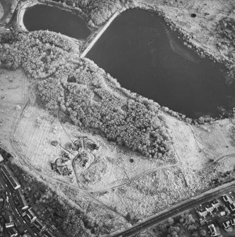 Oblique aerial view centred on the remains of the four gun-emplacements, command and control building, electric generator engine house and magazines, with the remains of two additional gun emplacements to the SW and rig adjacent, taken from the W.