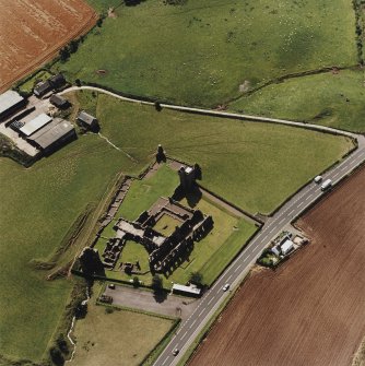 Oblique aerial view centred on the remains of the abbey and the doocot and cottage, taken from the NE.